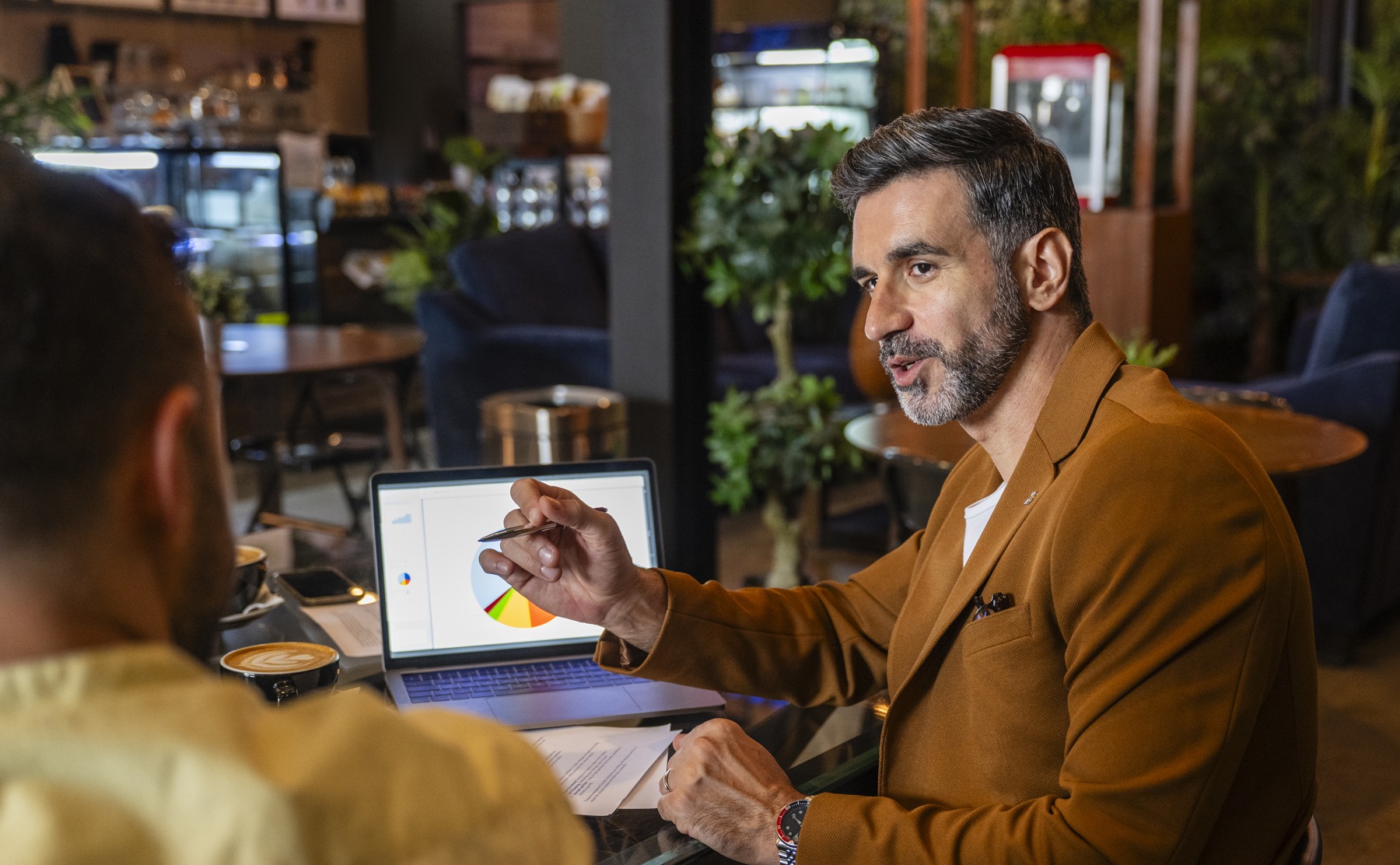 Man in a suit sitting on a desk and speaking to another person