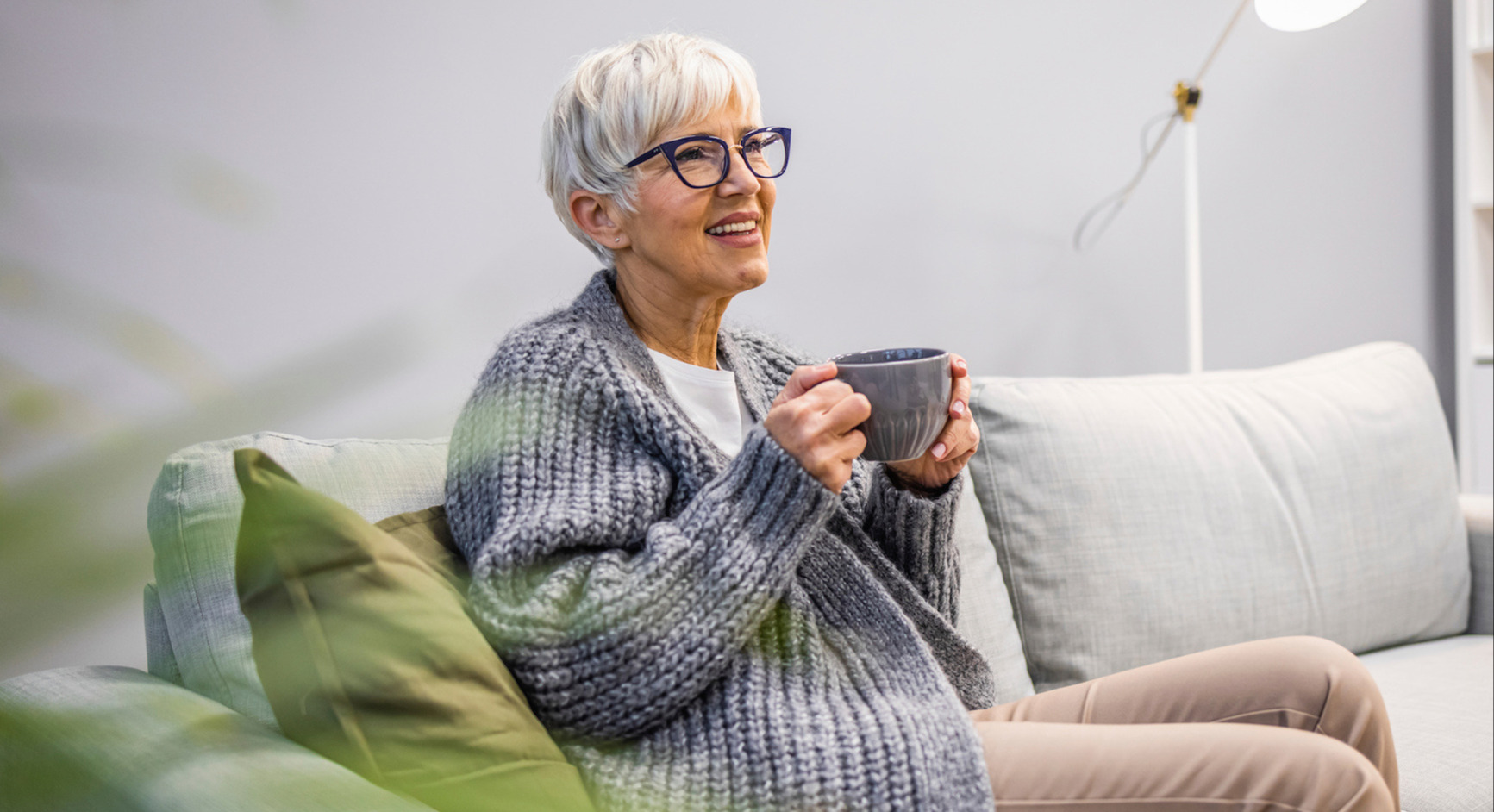 An elderly woman sitting on a sofa and drinking tea
