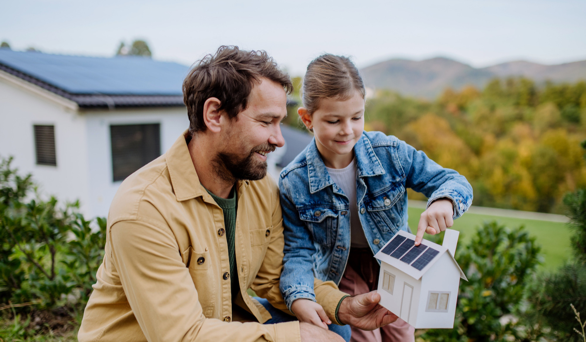 Little girl with her dad holding paper model of house with solar panels