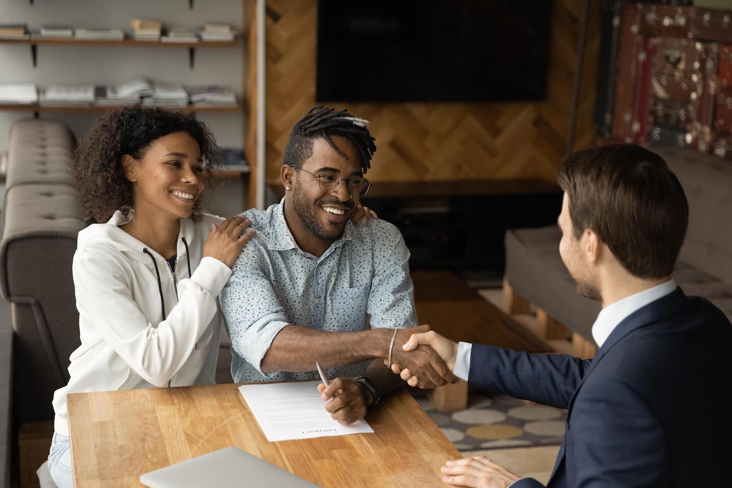 A couple handshaking a broker in an office