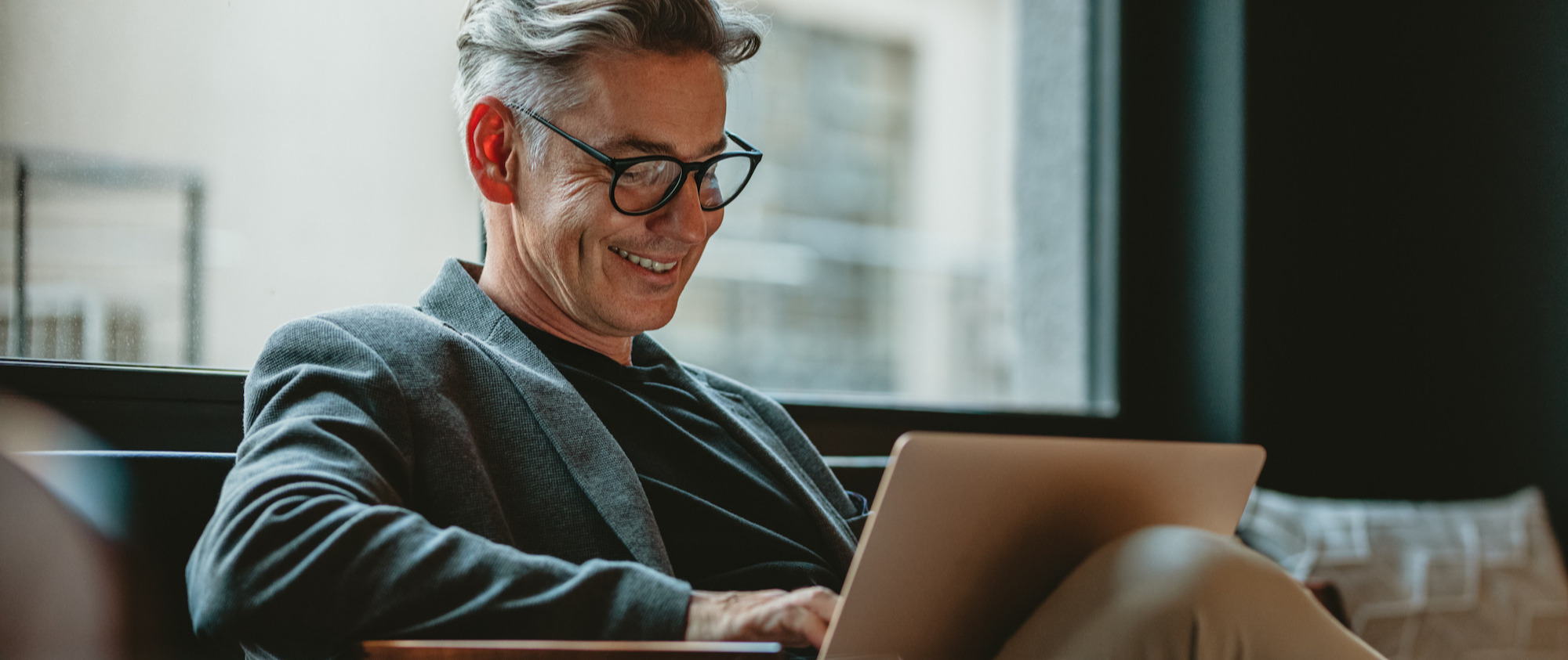 A smiling man typing on a laptop in a coffee shop