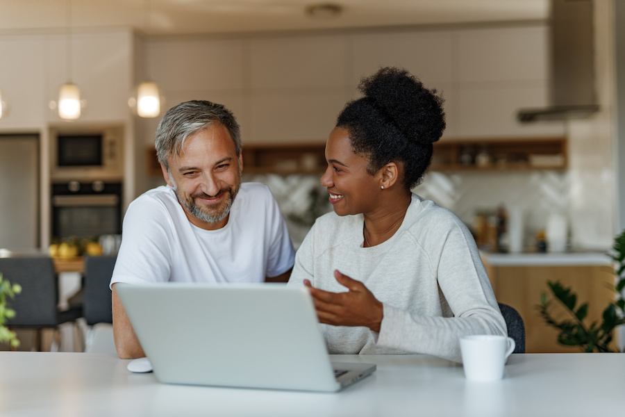 Interracial couple laughing at home in front of laptop