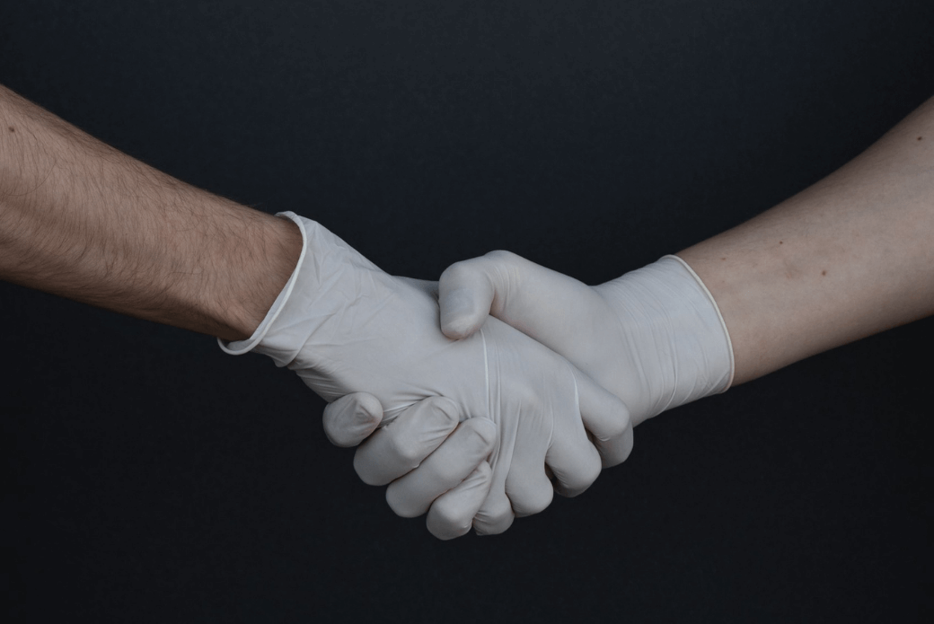 Two people shaking hands wearing gloves